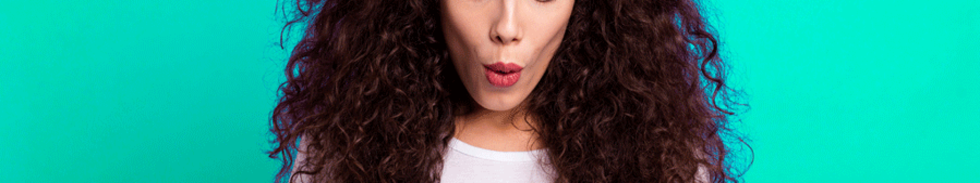 femme aux cheveux bouclés sur un fond vert qui tient sans téléphone entre ses mains et qui a une mine surprise