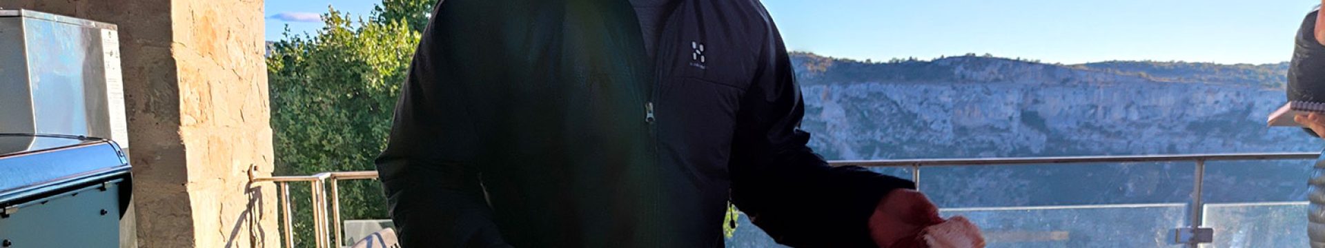 homme brun en train de découper un morceau de viande tendre. En fond se trouve un beau paysage naturel.